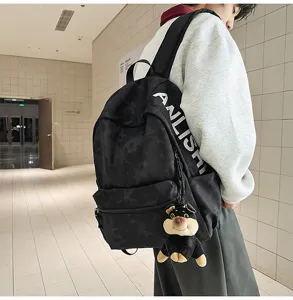 Detail view of a large-capacity black casual backpack with printed text strap and a cute dog pendant.