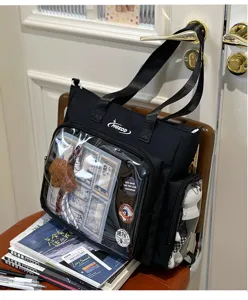 Detailed shot of black canvas itbag with clear front window, badges and cute plush toy.