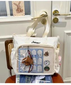Japanese ins style white canvas ita bag with transparent front pocket, pins and plush pendant.