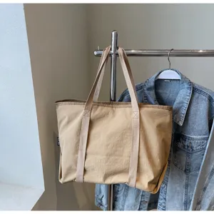Detail view of casual khaki tote bag hanging on metal rack with denim jacket, minimalist.