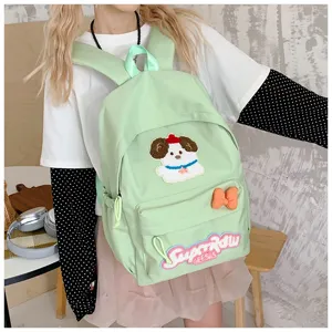 Close-up detail of the light green cute dog embroidered backpack showing front pocket and patch.
