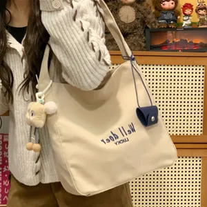 Nahaufnahme der beigen Segeltuch-Totetasche mit süßem Buchstabenstick und Anhänger.