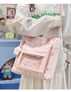 Rosa Canvas Ita Umhängetasche mit transparenter Fronttasche, Sternenmuster und Plüschanhänger.