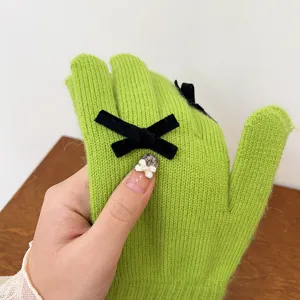 Detailed view of the green knit winter gloves featuring a chic black bow decoration.