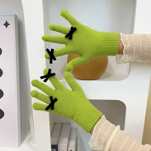 Close-up view of vibrant green knitted gloves featuring elegant black bowknot details on fingers.
