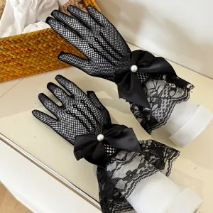 Close up detail of black fishnet lace gloves featuring elegant satin bow and pearl accent.