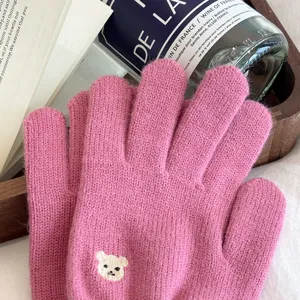 Close-up detail of cozy pink knit gloves featuring cute embroidered bear accent in lifestyle setting.