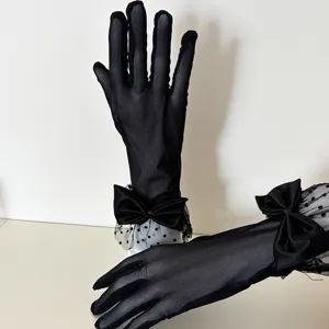 Close-up detail of black sheer mesh polka dot gloves featuring elegant satin bow decoration.