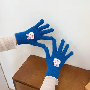 Close-up detail of blue knitted gloves featuring cute 3D cartoon rabbit patch and lace cuff.