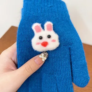 Close-up detail of winter warm blue knitted gloves featuring a cute white bunny plush decoration.