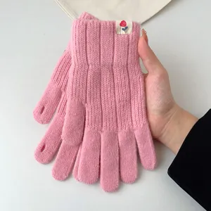 Close-up detail of pink knitted winter gloves with ribbed cuff and cute floral label.