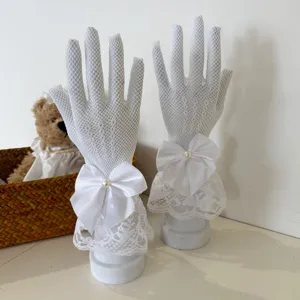 Detail view of white fishnet lace gloves featuring elegant satin bow and pearl ornament.