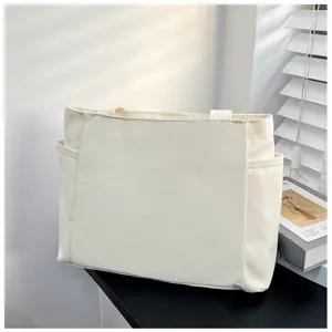Nahaufnahme einer minimalistischen weißen Canvas-Tasche mit Seitentaschen auf schwarzem Tisch.