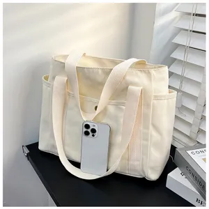 Detailansicht einer minimalistischen, beigen Segeltuchtasche mit Seitentaschen und Griffen.