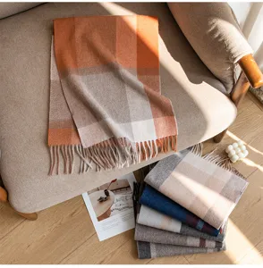 Detail view of cozy autumn winter plaid cashmere scarf with fringes on armchair and floor.
