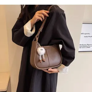 Detailed shot of trendy brown leather underarm shoulder bag featuring a cute fluffy pendant.