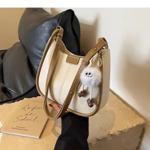 Detail view of a stylish two-tone underarm shoulder bag with cute furry charm and brown trim.