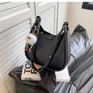 Detail shot of stylish black leather shoulder bag with cute fuzzy charm and prop book decor.