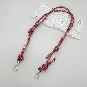 Detailed view of colorful woven bag strap accessory with metal clasps on a white wavy prop.