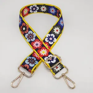 Détail de bandoulière de sac colorée à fleurs, large sangle avec accessoires en métal doré.