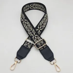 Detailed view of the wide black embroidered bag strap with golden metal hardware and hooks.
