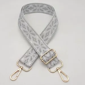 Primo piano della tracolla ricamata geometrica grigia con accessori in metallo dorato.