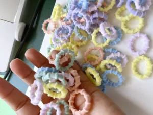 Detail view of colorful small hair ties in hand, showing soft texture and pastel colors.
