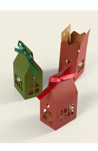Close-up detail of Christmas house shaped paper gift boxes with cutout windows and ribbons.