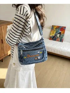 Detail view of multi-compartment denim crossbody bag with cute embroidery and zippers.