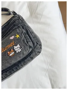 Close-up of cute cat embroidered denim crossbody bag pocket, multi-compartment style detail.