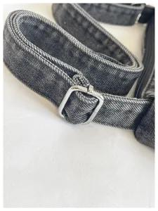 Close-up view of the denim bag strap with metal adjustable buckle, fine texture and stitching.