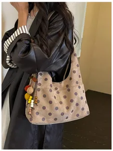Detail view of stylish polka dot underarm shoulder bag with cute hanging charms and suede texture.