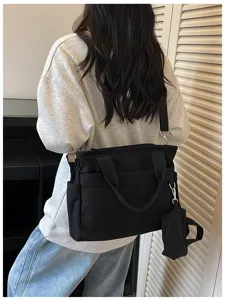 Vue détaillée d'un sac bandoulière en toile noire avec poignées et petite pochette.