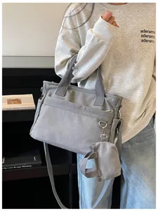 Détail de sac bandoulière en toile grise avec plusieurs poches et petite poche attachée.