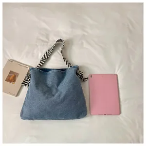 Vista dettagliata della borsa a tracolla in denim casual con eleganti cinturini a righe su sfondo.