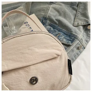 Close-up detail of beige nylon shell crossbody bag pocket texture and metal logo accent.