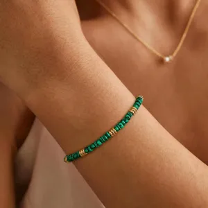 Close-up detail of a green stone beaded bracelet with gold spacer rings on wrist.