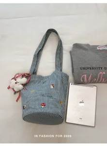 Detailansicht der gestreiften Canvas-Eimerentasche mit süßer Stickerei und Alltagsaccessoires.
