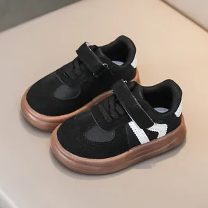 Close up of black children sneakers with brown sole, velcro strap and side stripe details.