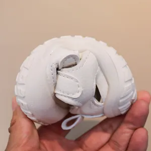 Flexible white toddler sandal detail showing soft sole bending and velcro closure design.