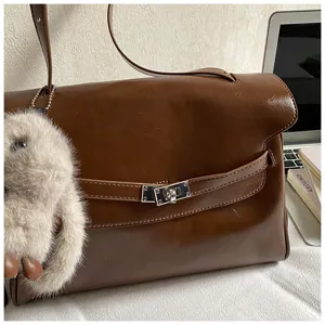 Sac à bandoulière vintage marron avec fermeture à tour et pendentif en peluche duveteuse.