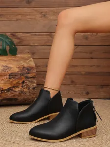 Gros plan de bottines noires à talons bas, découpe en V sur le côté et fermeture éclair au dos.