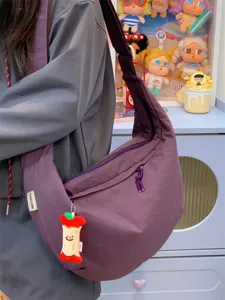 Vue détaillée d'un grand sac bandoulière en nylon violet avec charmant pendentif pomme.