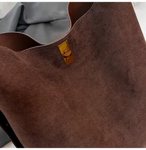 Close-up detail of retro brown suede women bucket bag with gold turn-lock hardware texture.