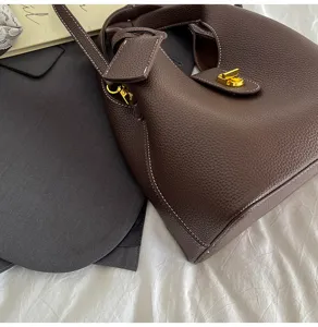 Brown leather bucket bag closeup detail, featuring shiny gold metal lock and shoulder strap.