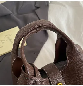 Close-up detail shot of brown textured leather handbag handle, featuring elegant contrast stitching.