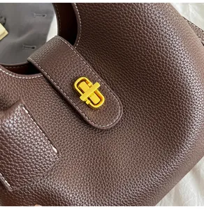 Brown leather bucket bag detail showing premium texture gold tone turn lock and white stitching close up
