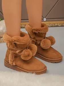 Close-up detail of cozy brown snow boots featuring plush faux fur trim and cute ribbon pom-poms.
