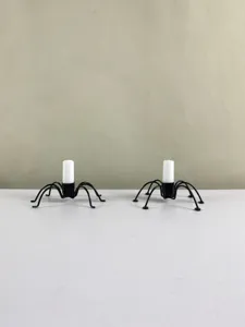 Close-up detail of black metal spider candle holders with white candles for spooky decor.