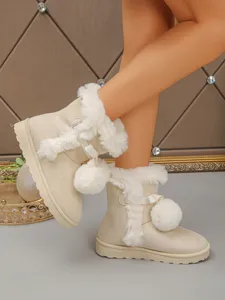 Detail view of beige fluffy snow boots with cute bow and pom-pom decor for cozy winter wear.